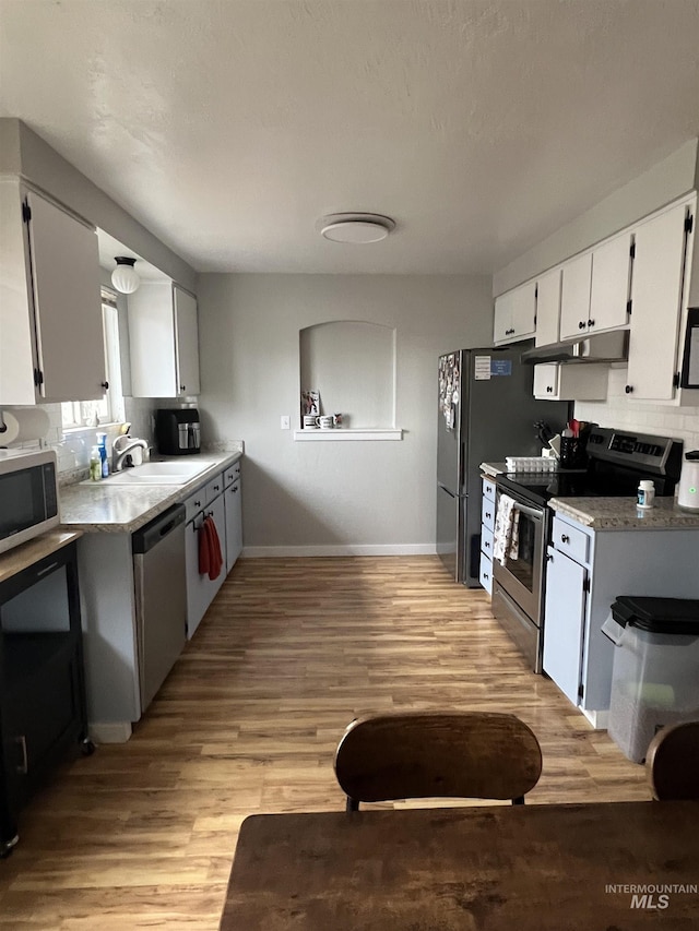 kitchen with stainless steel appliances, white cabinetry, light hardwood / wood-style floors, and sink