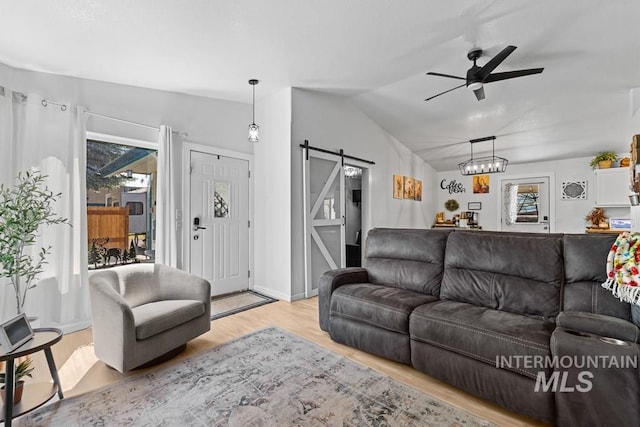 living room featuring a barn door, ceiling fan, lofted ceiling, and light hardwood / wood-style flooring