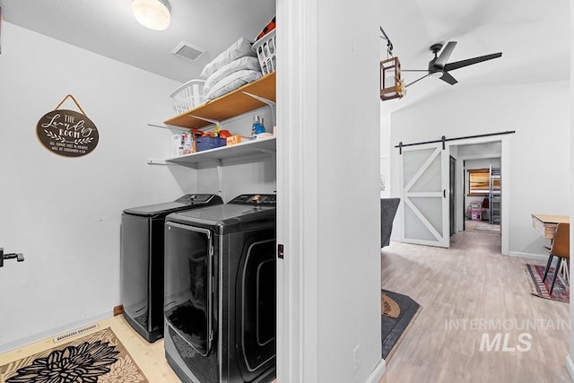 laundry area featuring a barn door, ceiling fan, light wood-type flooring, and separate washer and dryer