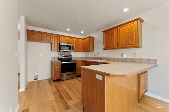 1406 W Wright St, Boise, ID 83705 - kitchen featuring stainless steel appliances, a sink, a peninsula, brown cabinetry, and light wood-style flooring