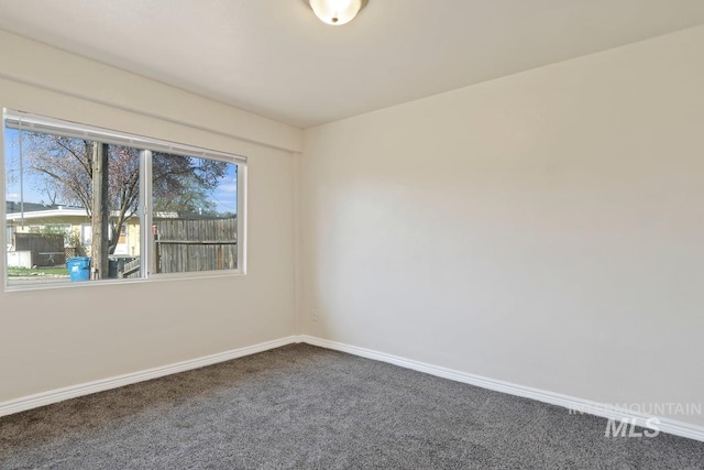 spare room featuring baseboards and dark carpet