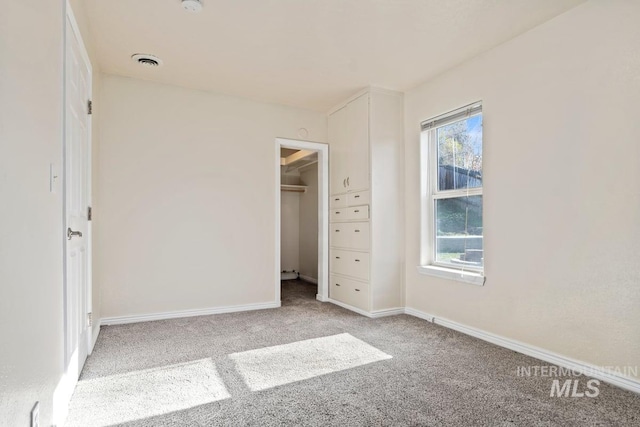 unfurnished bedroom featuring a walk in closet, baseboards, visible vents, and carpet flooring