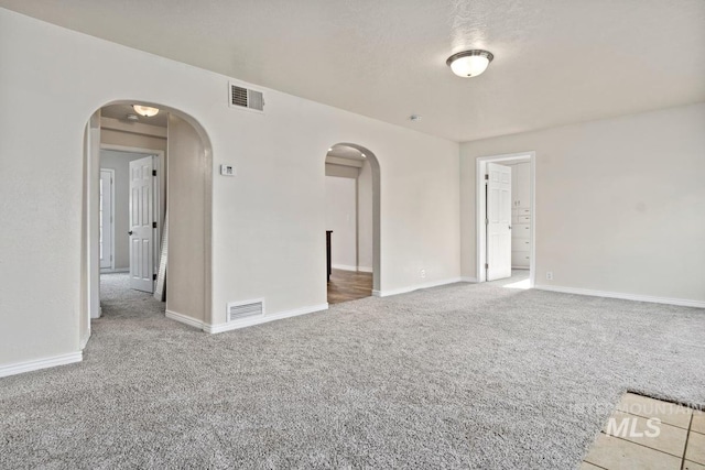 unfurnished room featuring arched walkways, visible vents, and carpet