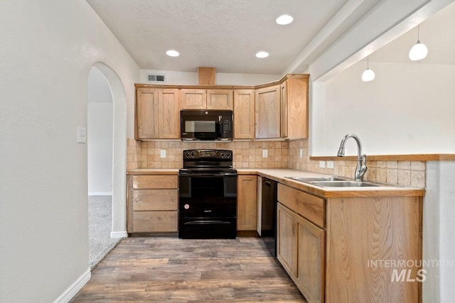 kitchen with light brown cabinetry, decorative backsplash, a sink, black appliances, and wood finished floors