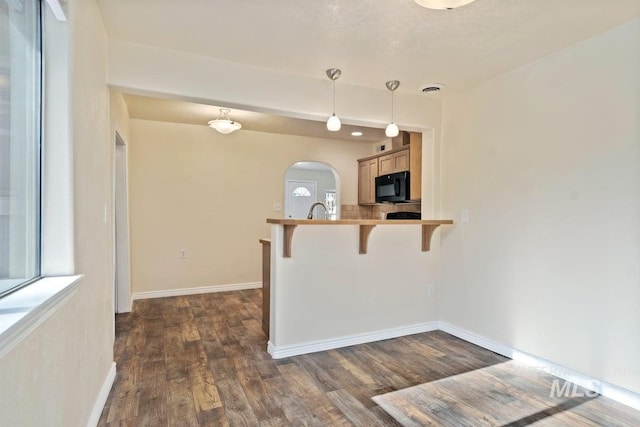 kitchen with dark wood-style flooring, baseboards, arched walkways, black microwave, and a breakfast bar area
