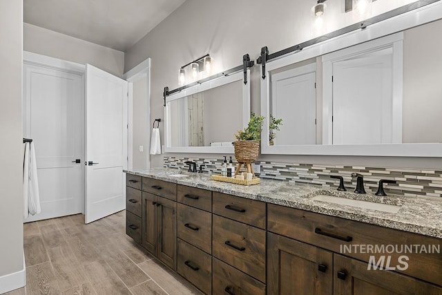 full bath with tasteful backsplash, double vanity, wood finished floors, and a sink