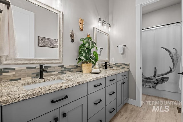 bathroom featuring double vanity, decorative backsplash, wood finished floors, and a sink