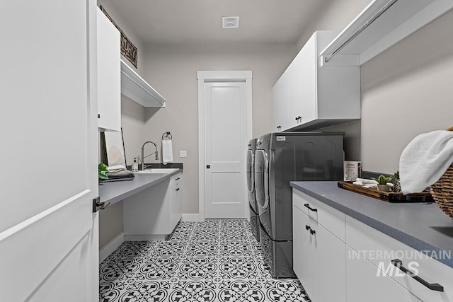 laundry area with baseboards, light tile patterned floors, separate washer and dryer, cabinet space, and a sink