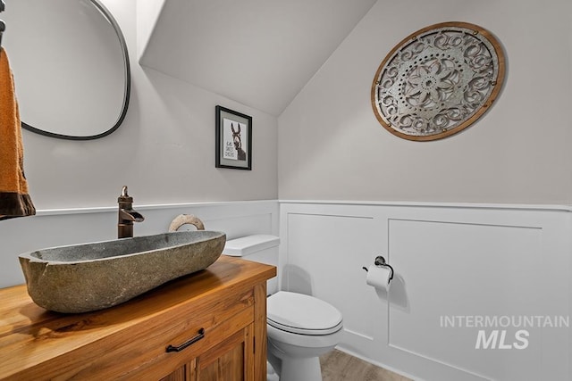 bathroom featuring a wainscoted wall, toilet, wood finished floors, lofted ceiling, and vanity