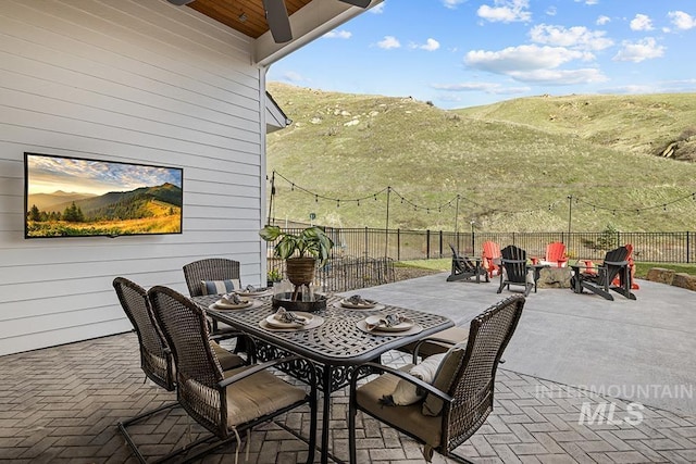 view of patio / terrace featuring outdoor dining space, a mountain view, a fire pit, and fence