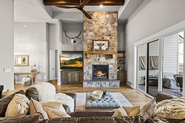 living room with a stone fireplace, beam ceiling, wood finished floors, and a ceiling fan