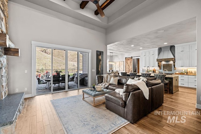 living area featuring ceiling fan, beamed ceiling, recessed lighting, light wood-style floors, and a towering ceiling