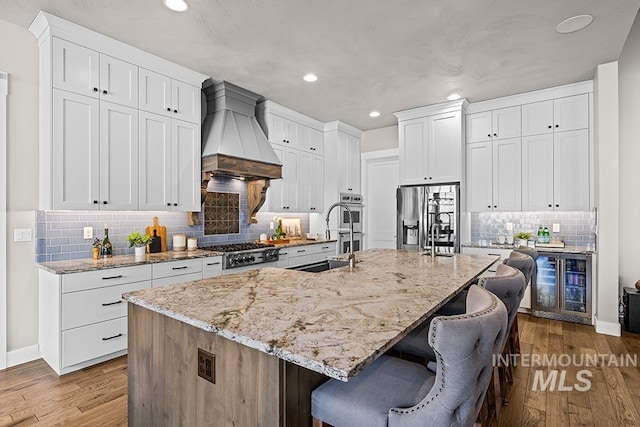 kitchen featuring premium range hood, a sink, wood finished floors, stainless steel appliances, and wine cooler