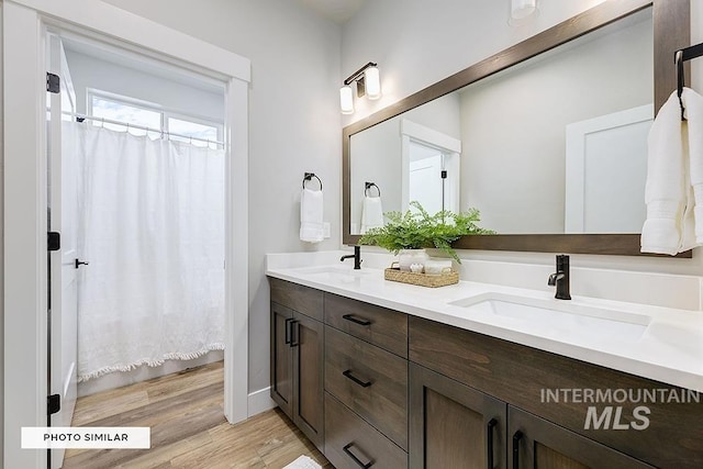 bathroom featuring a sink, double vanity, curtained shower, and wood finished floors