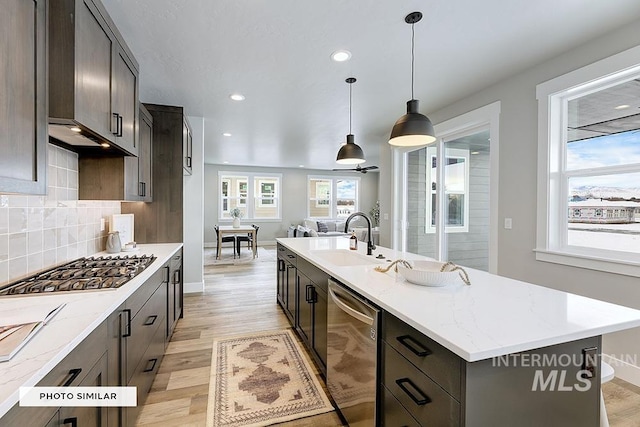 kitchen with stainless steel appliances, a center island with sink, light wood-type flooring, and a sink