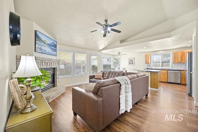 2189 W Rainfall St, Meridian, ID 83646 - living room with a ceiling fan, vaulted ceiling, light wood-style floors, a fireplace, and baseboards