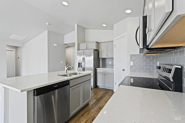 kitchen featuring dark wood finished floors, a kitchen island with sink, gray cabinetry, a sink, and appliances with stainless steel finishes