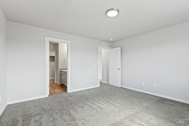 unfurnished bedroom with ensuite bath, visible vents, baseboards, and carpet