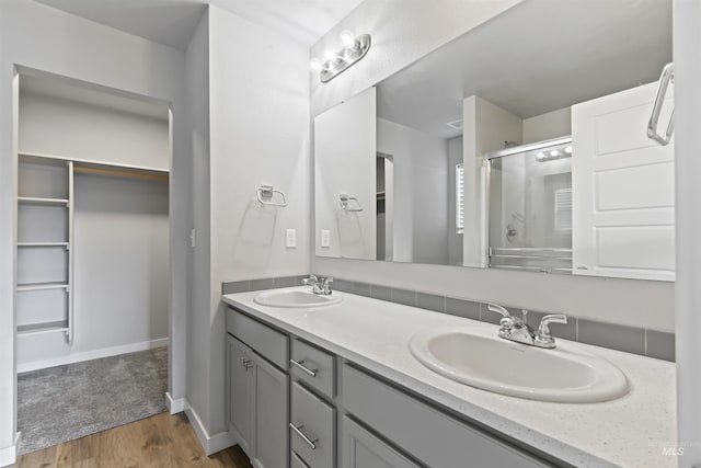 full bath featuring double vanity, wood finished floors, a shower with door, and a sink