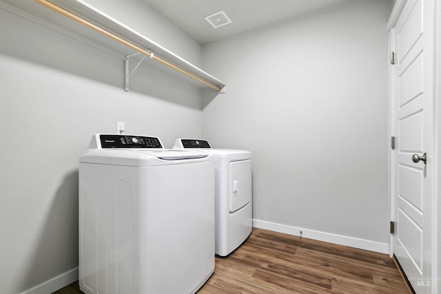 clothes washing area featuring wood finished floors, baseboards, visible vents, washing machine and clothes dryer, and laundry area