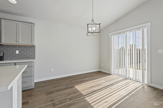 unfurnished dining area featuring dark wood-style floors, baseboards, an inviting chandelier, and vaulted ceiling