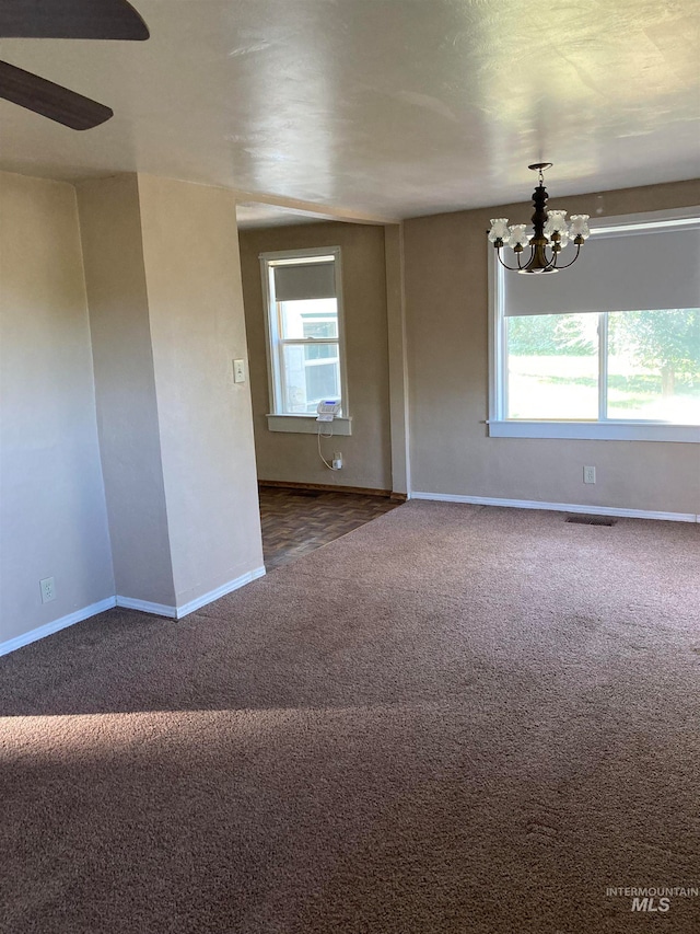 unfurnished room featuring carpet floors, ceiling fan with notable chandelier, and a wealth of natural light