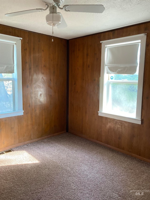 unfurnished room featuring wood walls, ceiling fan, and a healthy amount of sunlight