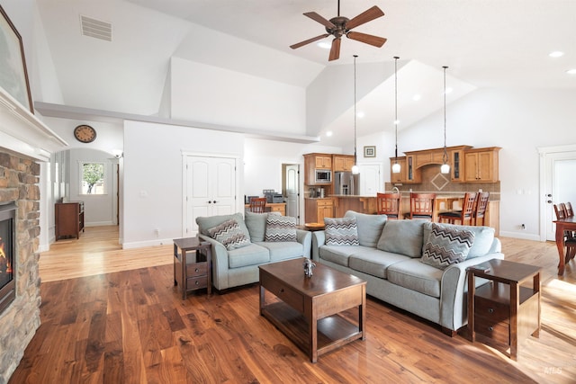 living room with a stone fireplace, visible vents, ceiling fan, high vaulted ceiling, and wood finished floors