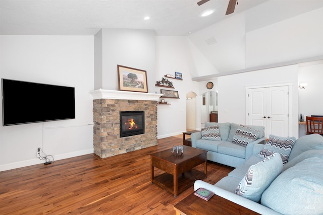 living room featuring ceiling fan, a stone fireplace, visible vents, wood finished floors, and baseboards
