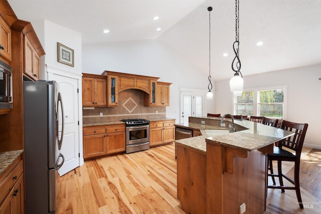 kitchen featuring light wood-type flooring, a kitchen breakfast bar, brown cabinets, stainless steel appliances, and backsplash