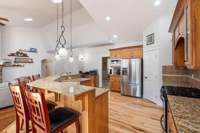 kitchen featuring backsplash, lofted ceiling, stainless steel appliances, light wood finished floors, and a sink