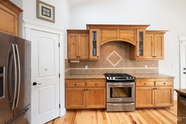 kitchen with tasteful backsplash, light stone counters, light wood-style floors, brown cabinetry, and stainless steel appliances