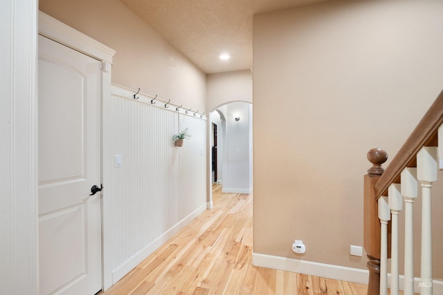 hallway with baseboards, light wood-type flooring, arched walkways, and stairs