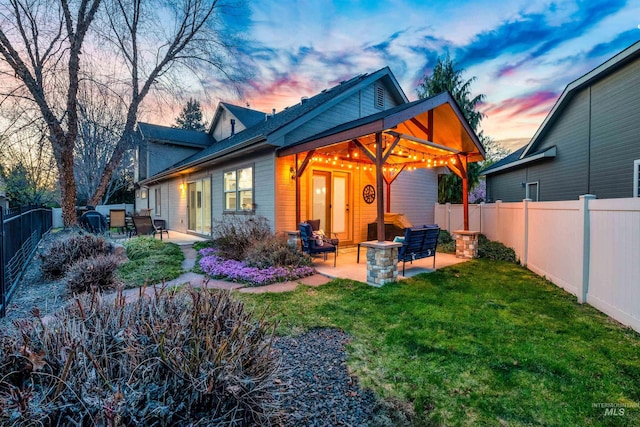 back of property at dusk featuring a patio, a fenced backyard, and a lawn