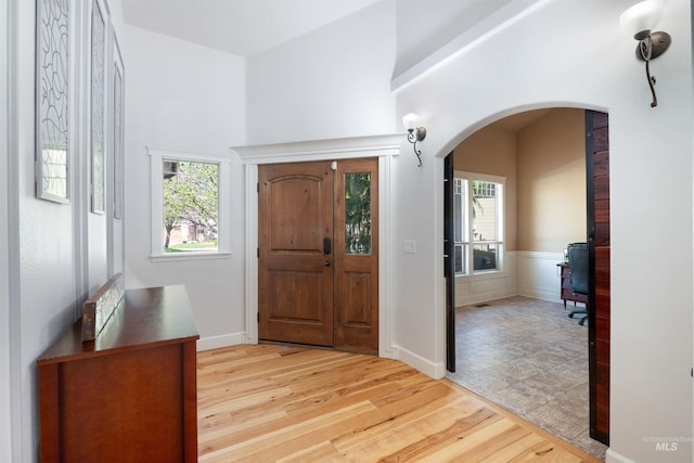 foyer entrance with arched walkways, plenty of natural light, and light wood-style floors