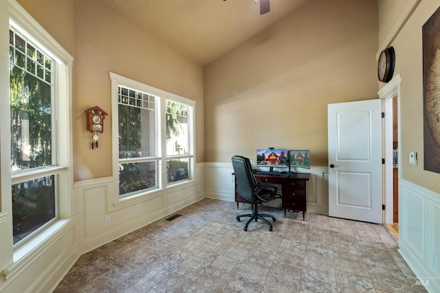 home office featuring a decorative wall, high vaulted ceiling, a ceiling fan, and wainscoting