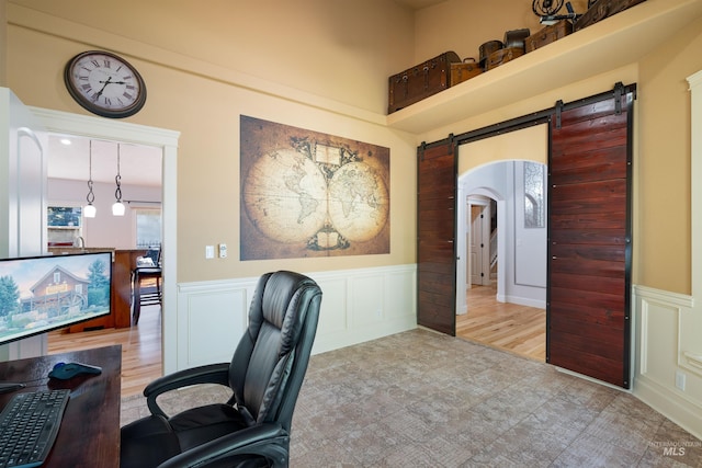 office area featuring arched walkways, a barn door, wainscoting, and a decorative wall