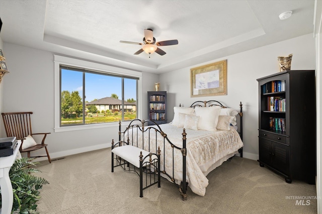 bedroom with ceiling fan, carpet floors, and a tray ceiling