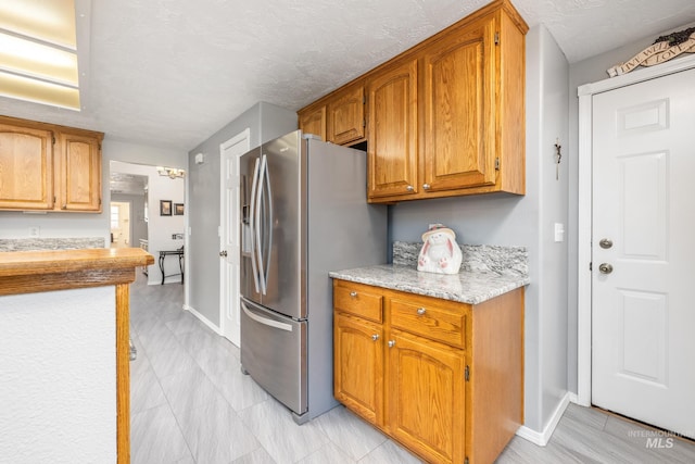 kitchen featuring stainless steel fridge, baseboards, brown cabinetry, and a textured ceiling