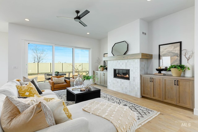 living room with visible vents, a tile fireplace, a ceiling fan, and light wood finished floors