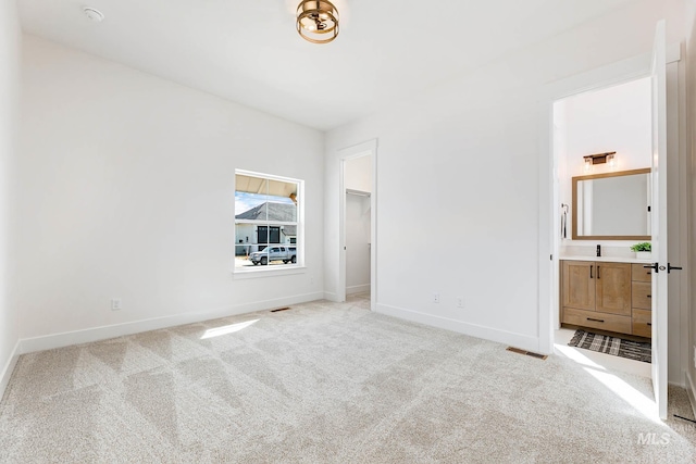 unfurnished bedroom with visible vents, light carpet, a walk in closet, connected bathroom, and baseboards