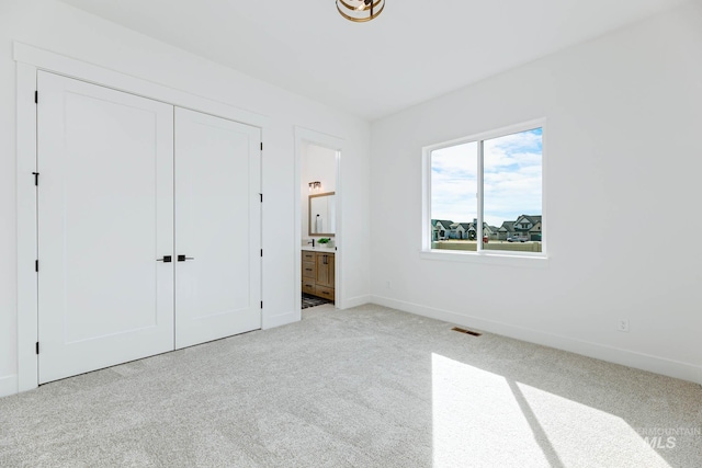 unfurnished bedroom featuring visible vents, baseboards, carpet flooring, ensuite bathroom, and a closet