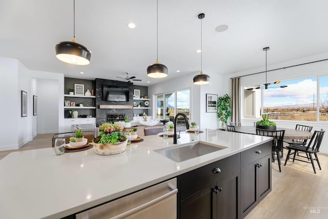 kitchen with light wood finished floors, a sink, a fireplace, light countertops, and dishwasher