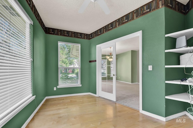 empty room with a textured ceiling, ceiling fan, wood finished floors, and baseboards