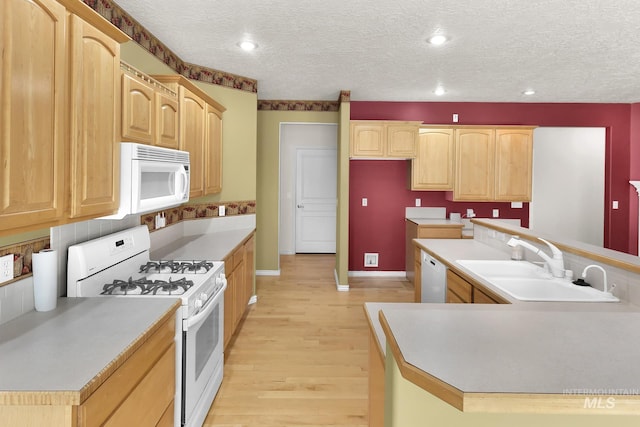 kitchen with white appliances, a sink, light brown cabinets, light wood-style floors, and baseboards