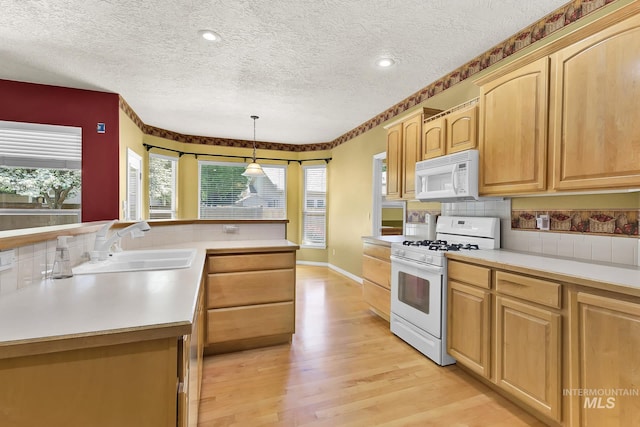 kitchen with white appliances, light wood finished floors, a textured ceiling, a sink, and light countertops