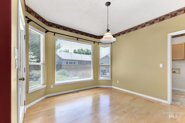 unfurnished dining area with a textured ceiling, light wood-style flooring, and baseboards