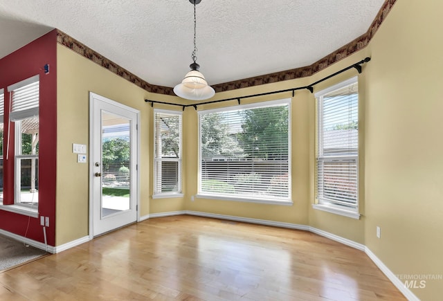 unfurnished dining area with a textured ceiling, wood finished floors, healthy amount of natural light, and baseboards