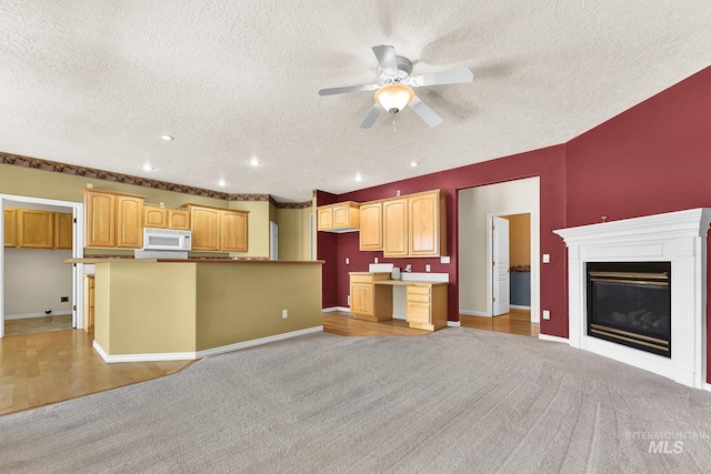 kitchen featuring white microwave, a textured ceiling, light colored carpet, ceiling fan, and a glass covered fireplace