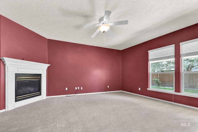 unfurnished living room with carpet, a textured ceiling, a ceiling fan, a glass covered fireplace, and baseboards